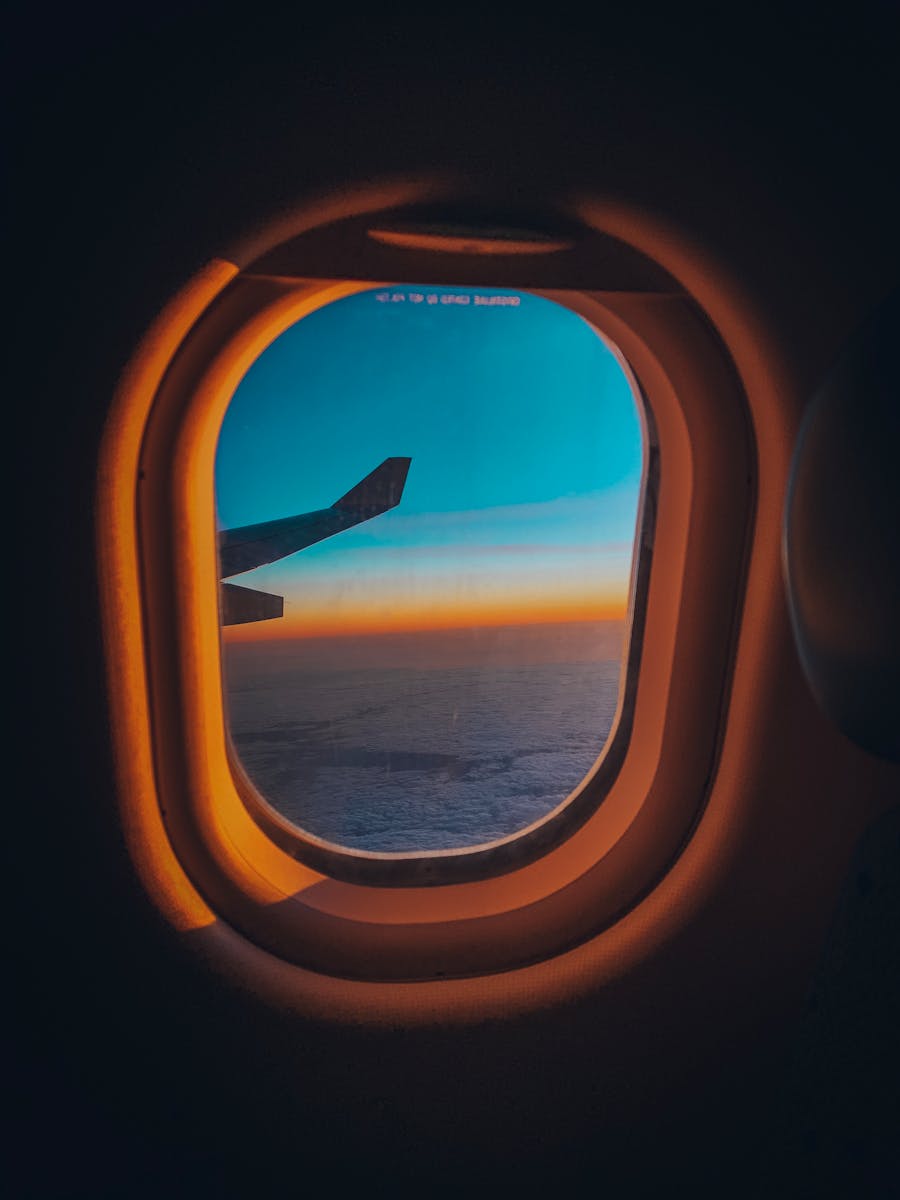 Experience the serene view from an airplane window overlooking a sunset sky and ocean horizon.