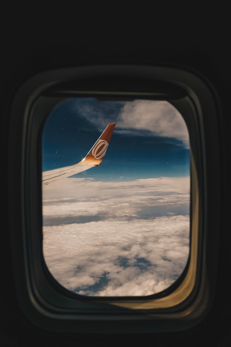 View of clouds and airplane wing from a window seat, offering a tranquil travel experience.